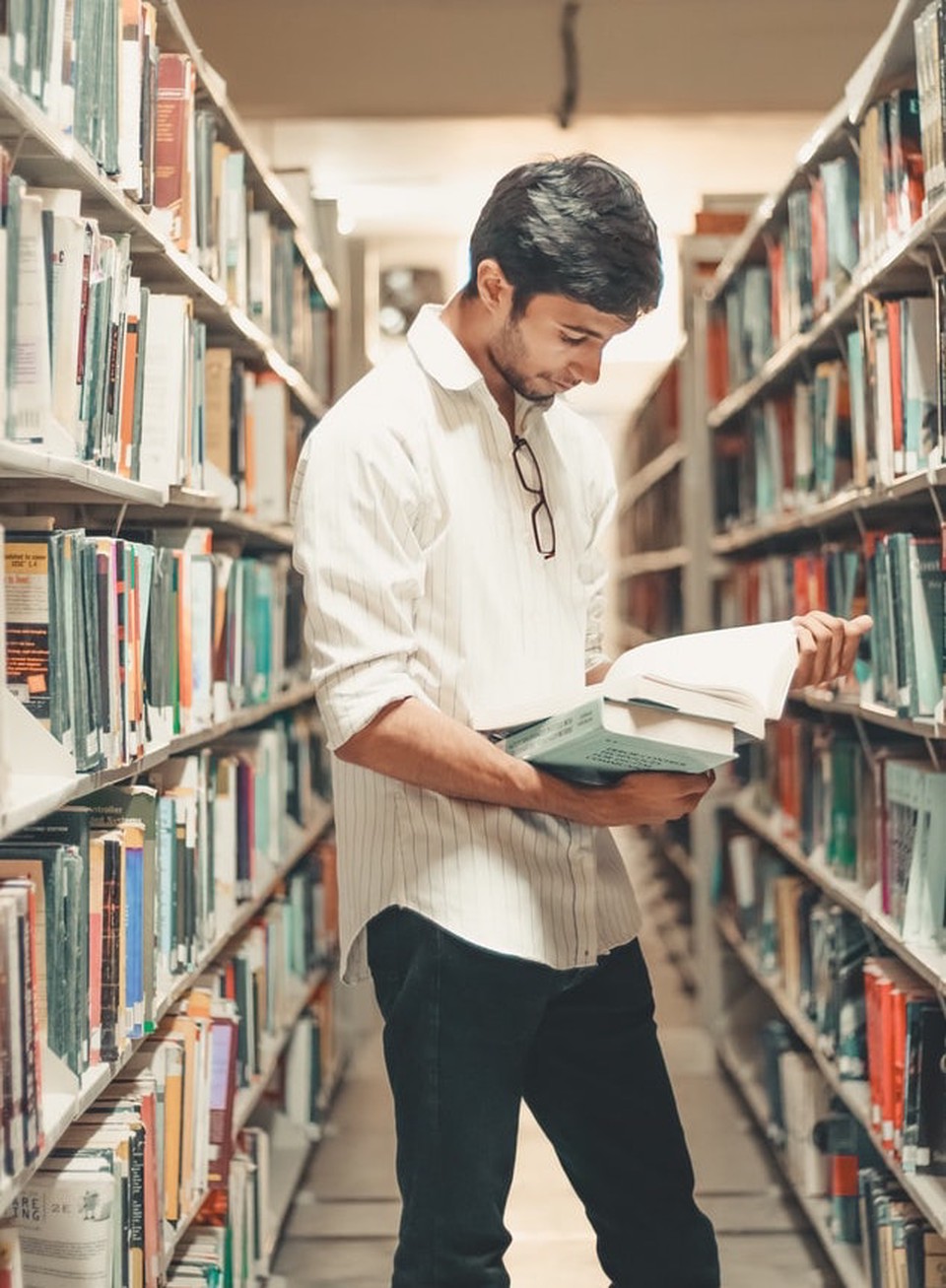 A man standing, reading a book inside a library